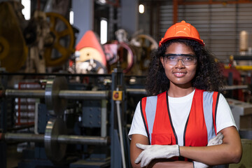 African women mechanical engineer, wearing safety equipment.  While do safety control while work inside of factory area. with heavy production machine inside factory at the background.