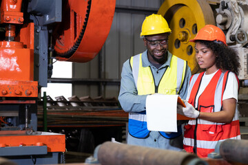 African mechanical engineer team, wearing safety equipment. While doing machine maintenance and safety control while work inside of factory area. With blurred background of heavy machine.