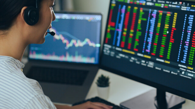 Young Asian woman broker wearing headphone, call center, customer service talking with customer and trading stock.