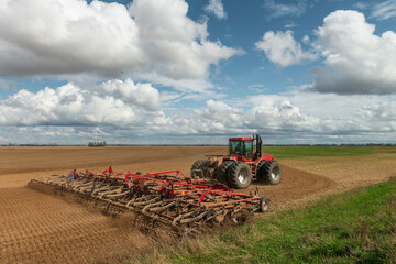 Red tractor cultivates the farm field. - 502055822