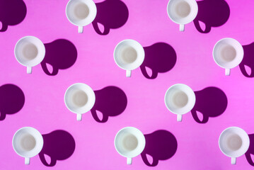Pattern of coffee cups from a top view casting a hard shadow with the silhouette of another cup....
