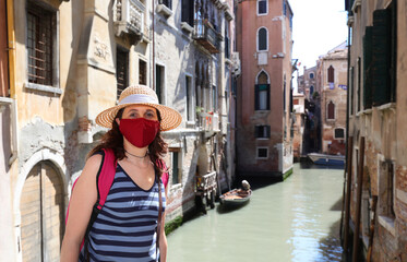 Fototapeta na wymiar young cute woman with straw hat and surgical mask is a curious tourist in Venice
