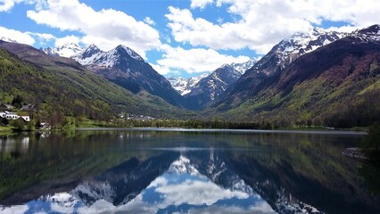 Fototapeta na wymiar Paysage d'un lac de montagne au pied des Pyrénées avec reflet du panorama et du ciel dans l'eau, et les maisons d'une petit village sur la rive gauche