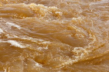 Fototapeta na wymiar Muddy river water. Dirty muddy water with whirlpool and white foam close-up.