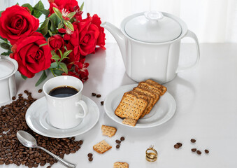 a pair of wedding rings on a table with, cup with coffee, wholegrain cookies on a saucer, on the table next to the window, light comes through the curtain and illuminates the table, red flower on the 