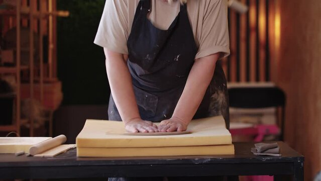 An eldery woman making a clay plate using a shape and big sponge stand