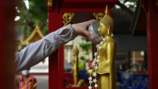 Woman hand pouring down scented water to Buddha statue during the Songkran festival in Thailand. This water festival marks the beginning of the traditional Thai New Year.