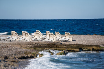 Empty beach chairs and closed  sun umbrellas on the beach in Greece.