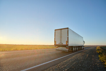 Semi-truck with cargo trailer driving on highway hauling goods in evening. Delivery transportation and logistics concept