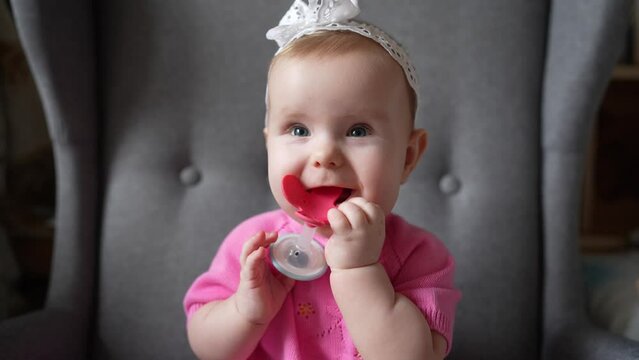 A baby girl european with blond hair bitting a teether toy and happily and sincerely smiles. Baby teething concept.