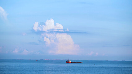 Breathtaking seascpe with a sailing red barge on blue cloudy sky on the background, water transport concept. Shot. Cargo ship barge on the sea horizon in a summer sunny day. - obrazy, fototapety, plakaty