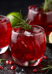 Pomegranate gin cocktail with lime, rosemary and ice on rustic black table