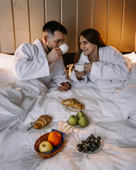 Happy young couple sitting in bed in morning and having breakfast