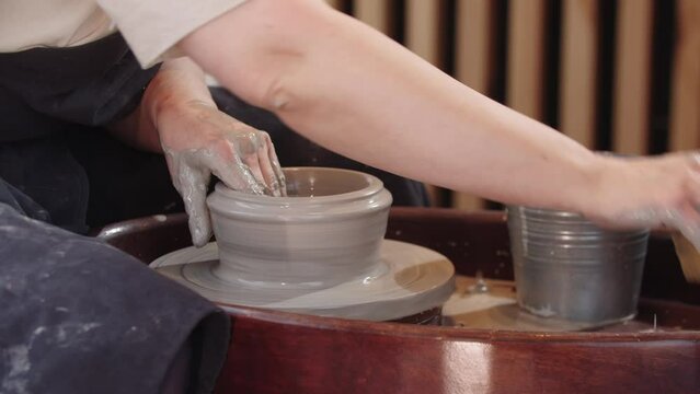 Hands of elderly woman widing a hole in piece of wet clay on the pottery wheel