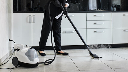 Cleaning service company employee removing dirt from floor in the kitchen with professional steam cleaner equipment