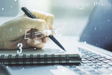 Double exposure of creative scientific formula concept with hand writing in notebook on background with laptop, research and development concept