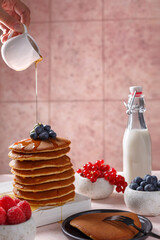 Pancakes sur une assiette couvert des fruits: framboise, myrtille. Sirop d'erable qui coule sur les...