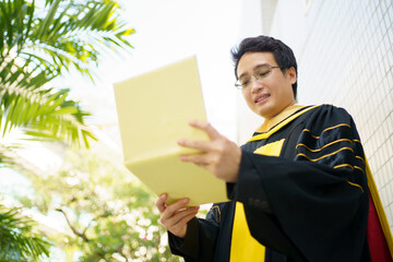 Happy Asian graduate student holding the diplomas on hand during the university graduation ceremony. 