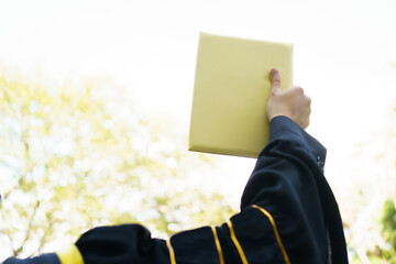 Happy Asian graduate student holding the diplomas on hand during the university graduation ceremony. Master degree student in gown suit holding a diplomas for photography.