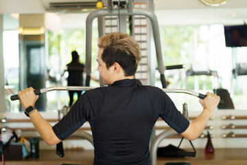 Fototapeta na wymiar Active young Asian sportsman practice weight training in the gym by using weight pulldown machine. 