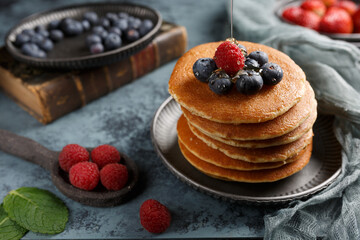 Pancakes sur une assiette couvert des fruits: framboise, myrtille. Le sirop qui coule sur les...