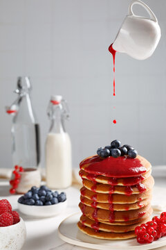 Coulis de fruits rouges sur les pancakes. Crêpes sur une assiette couvert de fruits rouges: myrtilles, framboises. Le bouteille de lait à coté.