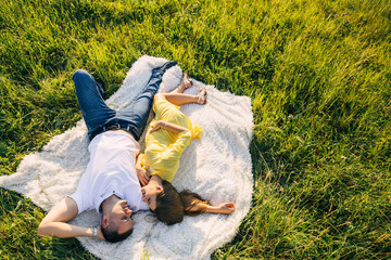 Pretty young pregnant woman with her handsome man is resting on a blanket in a summer meadow.