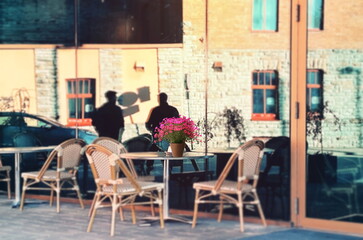 flowers on table top street cafe  building modern architecture windows and glass with stone and  people silhouette  in exit  urban city life Tallin