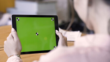 Fototapeta premium Rear view of a brunette woman using tablet with green screen, modern technologies concept. Stock footage. Female holding ipad with chromakey and reading something.