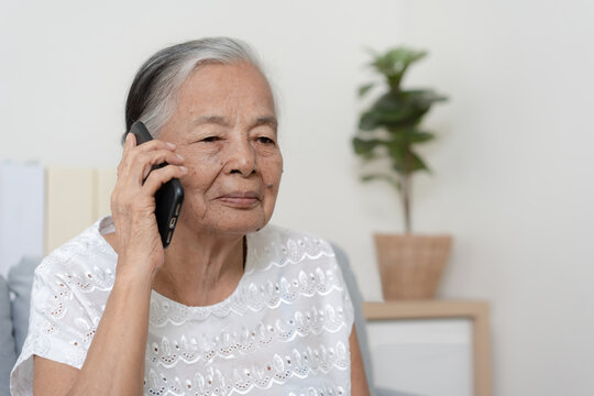 Happy Asian senior woman using  smartphone at home. Grandparent call to family member using mobile phone application.