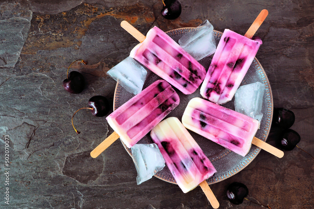Poster plate of healthy cherry yogurt ice pops. above view table scene over a dark stone background.