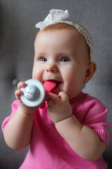 A baby girl european with blond hair bitting a teether toy and happily sincerely smiles. Baby...