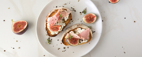 a plate of bruschettas with soft cheese, prosciutto and figs on a light table
