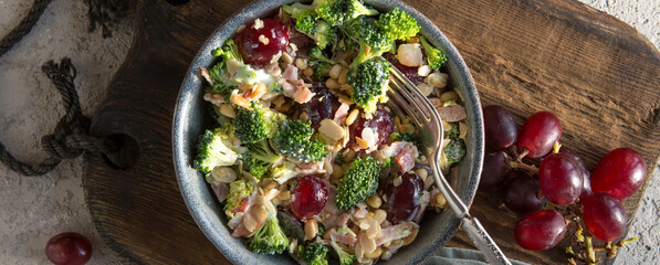 bowl with salad with broccoli, bacon, grapes and nuts on the table