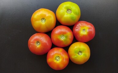 Bunch of healthy vegetable raw and ripe organic farm fresh red and yellow tomatoes isolated stacked together on black chopping board table background with copy space. Beautiful close up macro top view