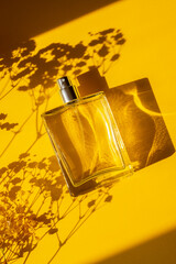 Transparent bottle of perfume on a yellow background. Fragrance presentation with daylight....