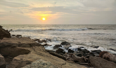 Fototapeta na wymiar Dramatic calm summer morning golden beach sunset with yellow and orange sunlight reflecting on kerala beach sea water waves, sky and rocks. Beautiful nature holiday and tourism wallpaper background.