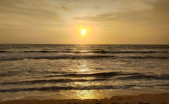 Dramatic calm summer evening golden beach sunset with yellow and orange sun light reflecting on kerala beach sea water waves, sky and sand. Beautiful nature holiday and tourism wallpaper background.