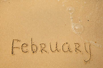 February - handwritten on the soft beach sand.