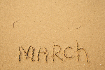 March - handwritten on the soft beach sand.