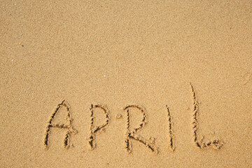 April - handwritten on the soft beach sand.