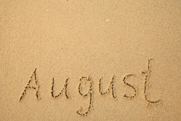 August - handwritten on the soft beach sand.