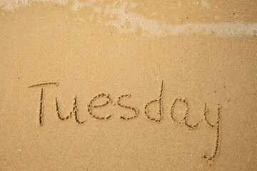 Tuesday - handwritten on the light beach sand with a soft wave lapping.