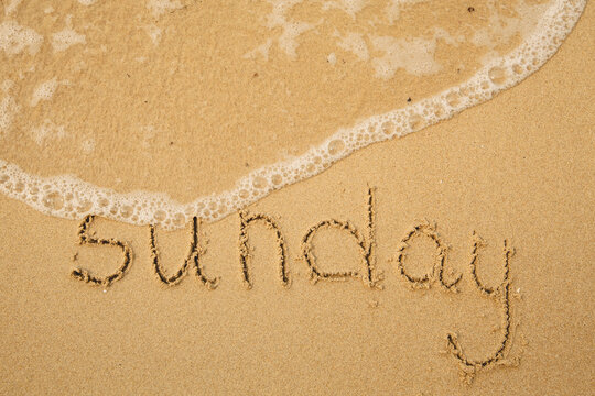 Sunday - handwritten on the light beach sand with a soft wave lapping.