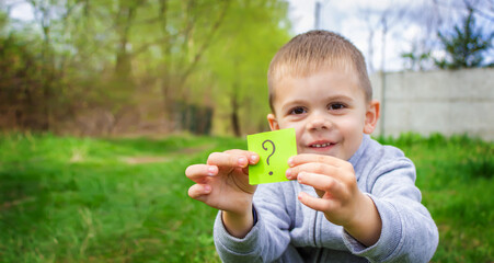 the boy holds stickers with a question mark on the background of the park. selective focus