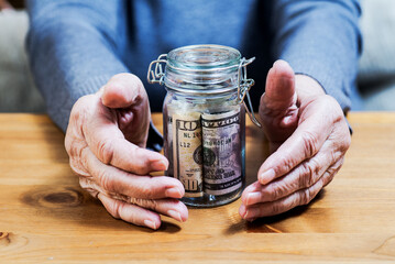 hands of an elderly woman keep banknotes in a small glass container.