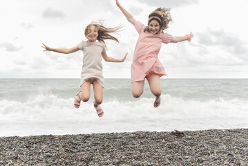 Two little girls in summer dresses are playing by the sea. Children walk along the seashore....