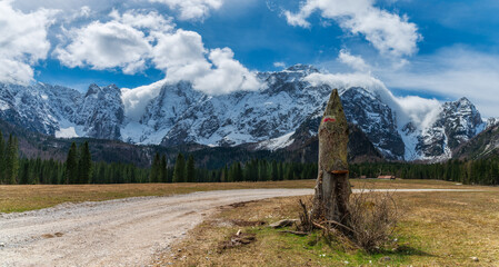 Path in the Valromana valley (Fusine), on the foreground a oath signal, on the background woods, forests and the Mountain Mangart (Italian Alps)