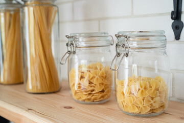 Wheat Italian pasta in glass jar on a wooden shelf in the kitchen.