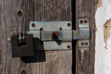 Old padlock, latch on wooden door with cracked texture. Close-up